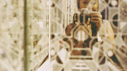 Photographer with camera reflected in mirror surrounded by reflective surfaces