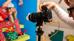 Photographer adjusting mirrorless camera on tripod during product photography shoot with colorful backdrop