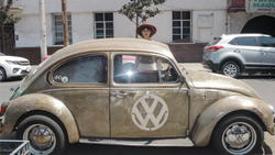 Vintage Volkswagen Beetle with patina finish and VW logo, driver visible through open window