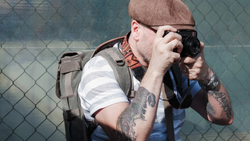 Photographer with camera and backpack shooting against chain-link fence