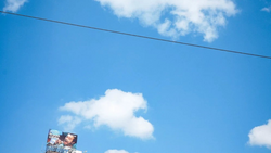 Billboard advertisement against bright blue sky with white clouds and power line