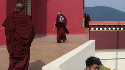 Buddhist monks in maroon robes walking across a courtyard with deep red walls and mountain backdrop