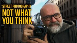 Bearded photographer holding compact camera on urban street with yellow text overlay