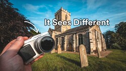 Hand holding a vintage rangefinder camera with a historic stone church and graveyard in the background