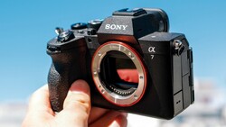 Sony α7 mirrorless camera held in hand against blue sky, showing red mirror box interior