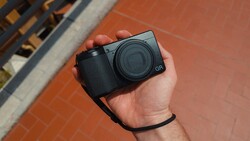 Ricoh GR compact camera held in hand against brick background
