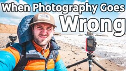 Photographer in blue and orange jacket holding camera on tripod at beach during golden hour