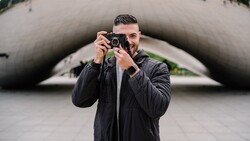 Photographer holding rangefinder camera to face while standing in front of curved concrete architectural structure