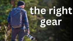 Photographer wearing backpack and beanie while holding telephoto lens in forest setting