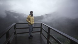 Person in yellow jacket standing on wooden observation deck overlooking misty forested mountains