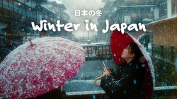 Person holding red umbrella in heavy snowfall on urban street with Japanese text overlay
