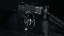 Black rangefinder camera with attached lens and shoulder strap on dark textured surface