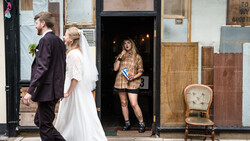 Bride and groom walking past storefronts with woman in doorway during street photography session