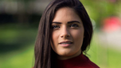 Portrait of a woman with long dark hair wearing a burgundy turtleneck against a blurred green background