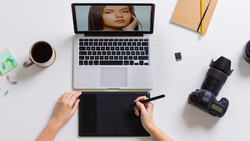 Photographer's overhead desk setup with laptop, graphics tablet, camera, and coffee