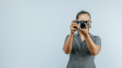 Photographer holding vintage film camera up to face against light blue background