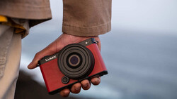 Person holding red Lumix compact camera with ocean backdrop