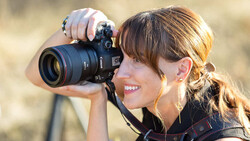 Female photographer holding a DSLR camera with telephoto lens, smiling while shooting outdoors