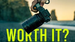 Hand holding a mirrorless camera with telephoto lens against coastal landscape at golden hour
