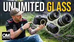 Photographer holding OM System camera with multiple lenses displayed outdoors