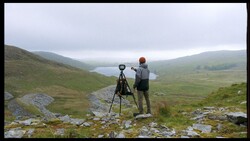 Photographer with tripod-mounted camera surveying mountainous valley landscape