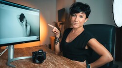 Female photographer at desk reviewing portrait on monitor with professional camera in foreground