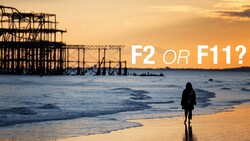Silhouetted figure wading in ocean at sunset with abandoned pier structure in background