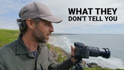 Photographer with telephoto lens on tripod overlooking coastal cliffs and ocean waves