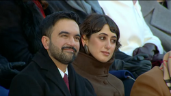Man and woman sitting together outdoors, dressed in dark winter coats