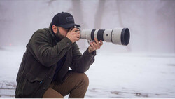 Photographer crouching while composing shot with telephoto lens
