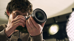 Photographer holding camera up to eye with both hands, shot from front with warm golden hour lighting