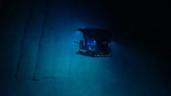 Submersible vessel illuminated by blue lights exploring the deep ocean floor