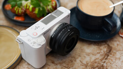 White mirrorless camera with black prime lens on textured surface surrounded by food styling props