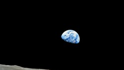 Earth rising above the lunar horizon against black space