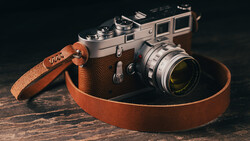 Vintage rangefinder camera with brown leather strap on dark wooden surface