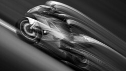 Black and white motion-blurred racing car leaning into a turn on a banked track
