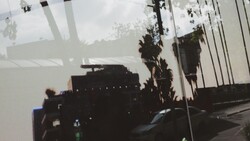 Double exposure of silhouetted buildings and palm trees overlaid with cloudy sky