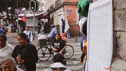 Busy urban street scene with pedestrians and a cyclist among market stalls and storefronts
