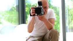 Bald man holding a medium format camera to his face, wearing a white t-shirt