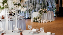 Elegant wedding reception setup with white linens, floral centerpieces, and cascading silver streamer backdrop