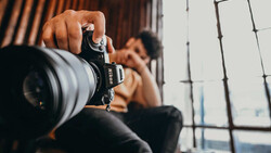 Photographer holding mirrorless camera with telephoto lens, shooting indoors with natural window light