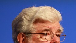 Older man with white hair and glasses against blue background