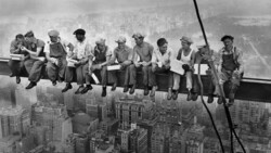 Workers perched on steel beams high above a cityscape during the construction of a skyscraper.