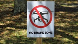 No Drone Zone sign with red prohibition symbol mounted on wooden post in outdoor park setting