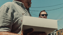 Two men examining a white cardboard box outdoors against a clear blue sky