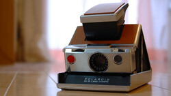 Polaroid SX-70 instant camera with flash attachment stacked on wooden base