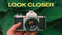 Asahi Pentax rangefinder camera held in hand against green foliage background