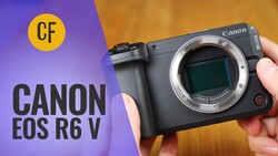 Canon EOS R6 V mirrorless camera body held in hand against purple and orange background