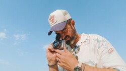 Photographer holding vintage rangefinder camera to eye against clear blue sky