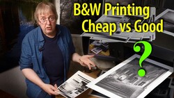 Man comparing black and white printed photographs at a desk with printers in background